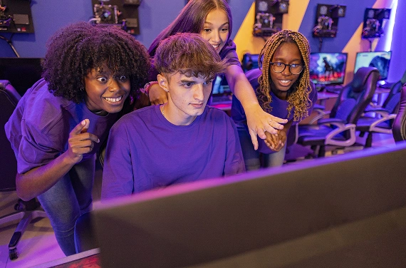 Un gruppo eterogeneo di giocatori che assiste insieme a una partita competitiva di eSport, reagendo alle azioni di gioco in un moderno centro dedicato al gaming dotato di potenti PC da gaming.